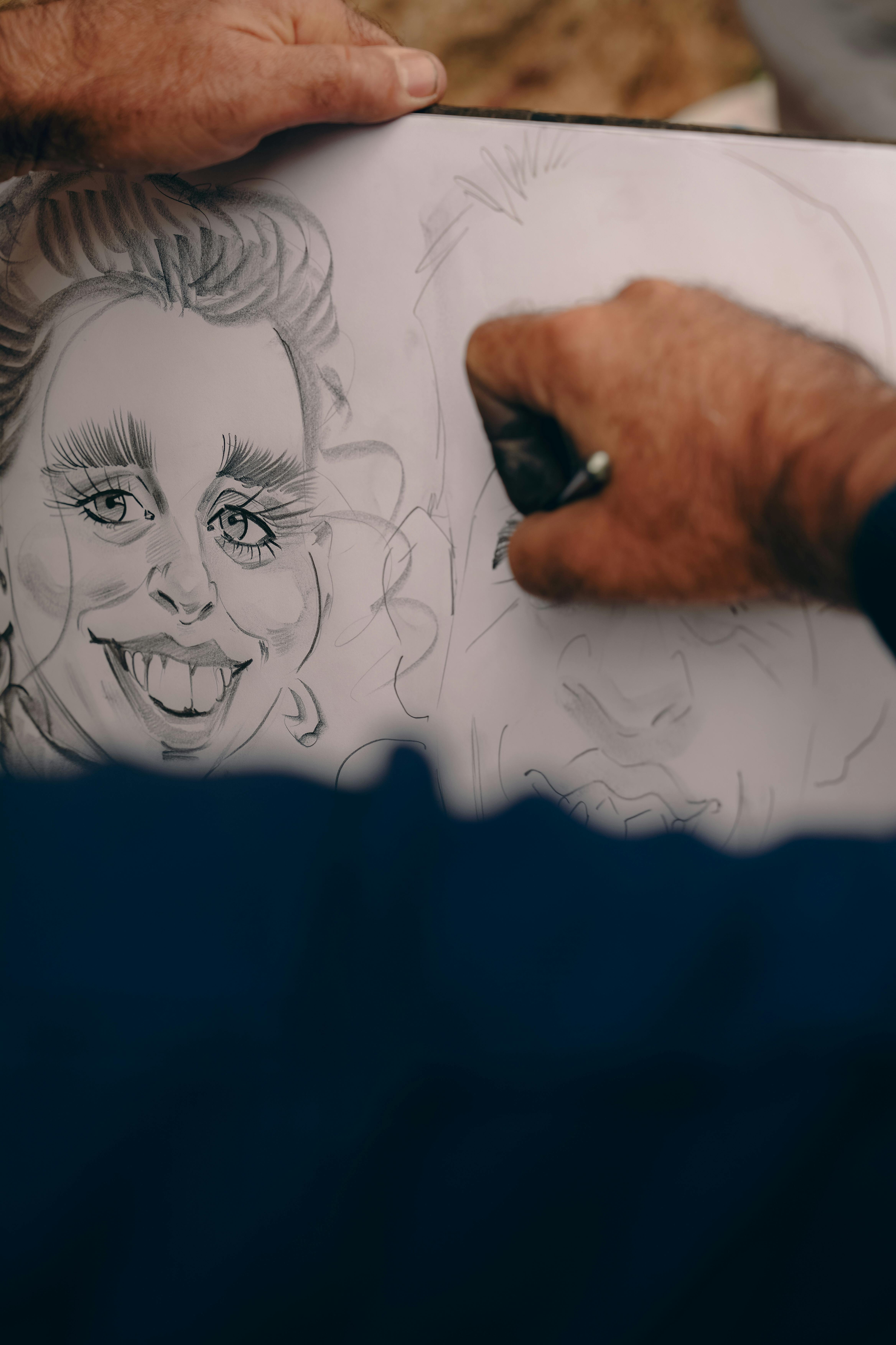 Close-up of hands drawing caricatures on paper, capturing creative artistry.