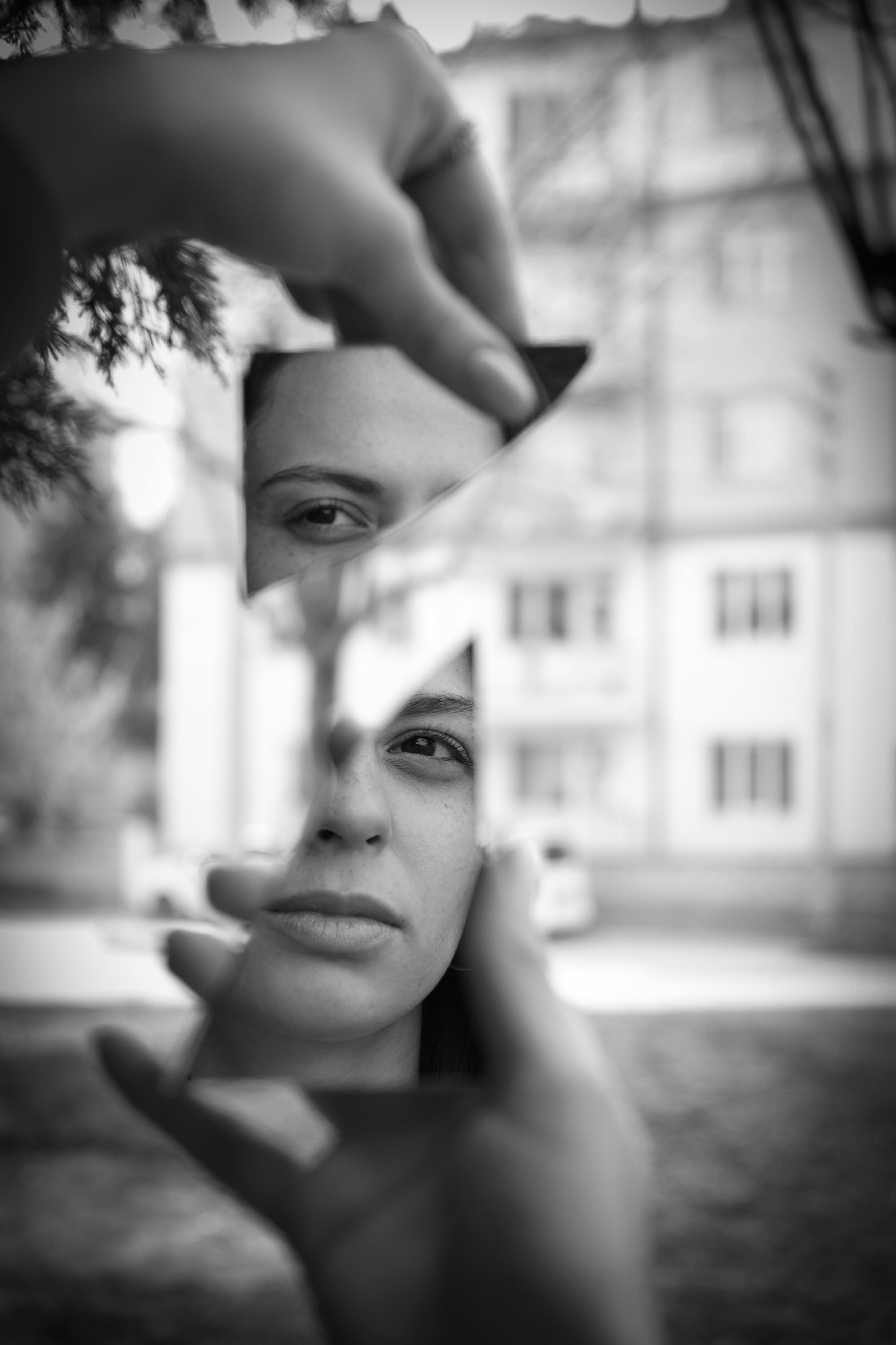 Artistic black and white portrait through broken mirror reflecting urban life.